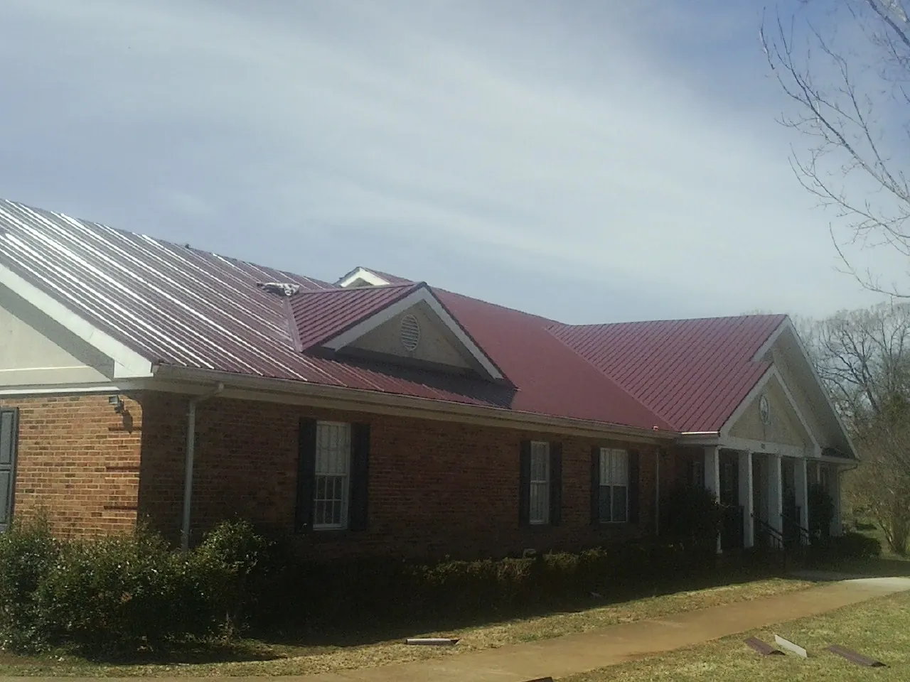 Red metal roof with gabled entries on a long brick building, from a Hail Damage Roof Repair job in Williamsville