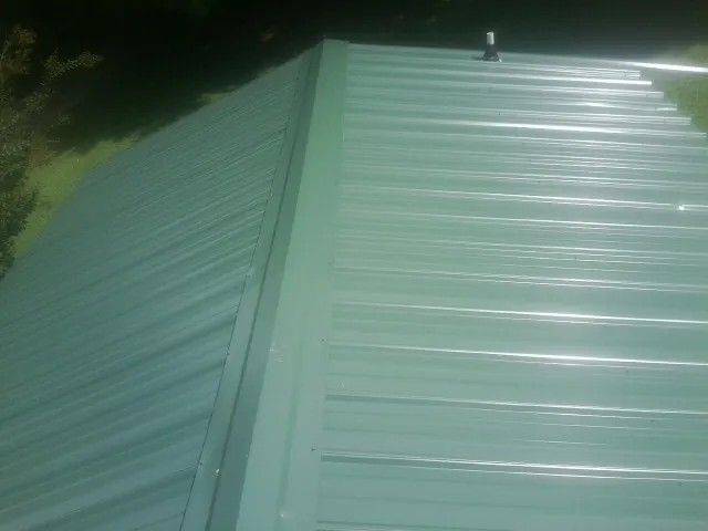 New green metal panels meeting at the ridge of a roof — Flat Roof Repair work by our crew in Williamsville