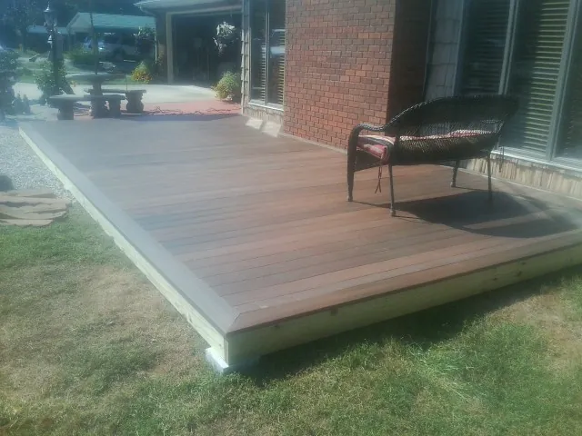 New wood deck and wicker chair beside a brick house in Williamsville