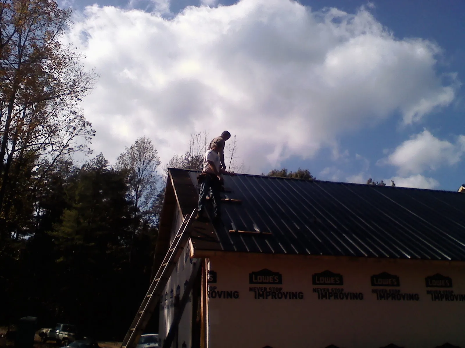 Roofer fastening dark metal panels high against a cloudy sky, from a Roof Inspection job in Williamsville