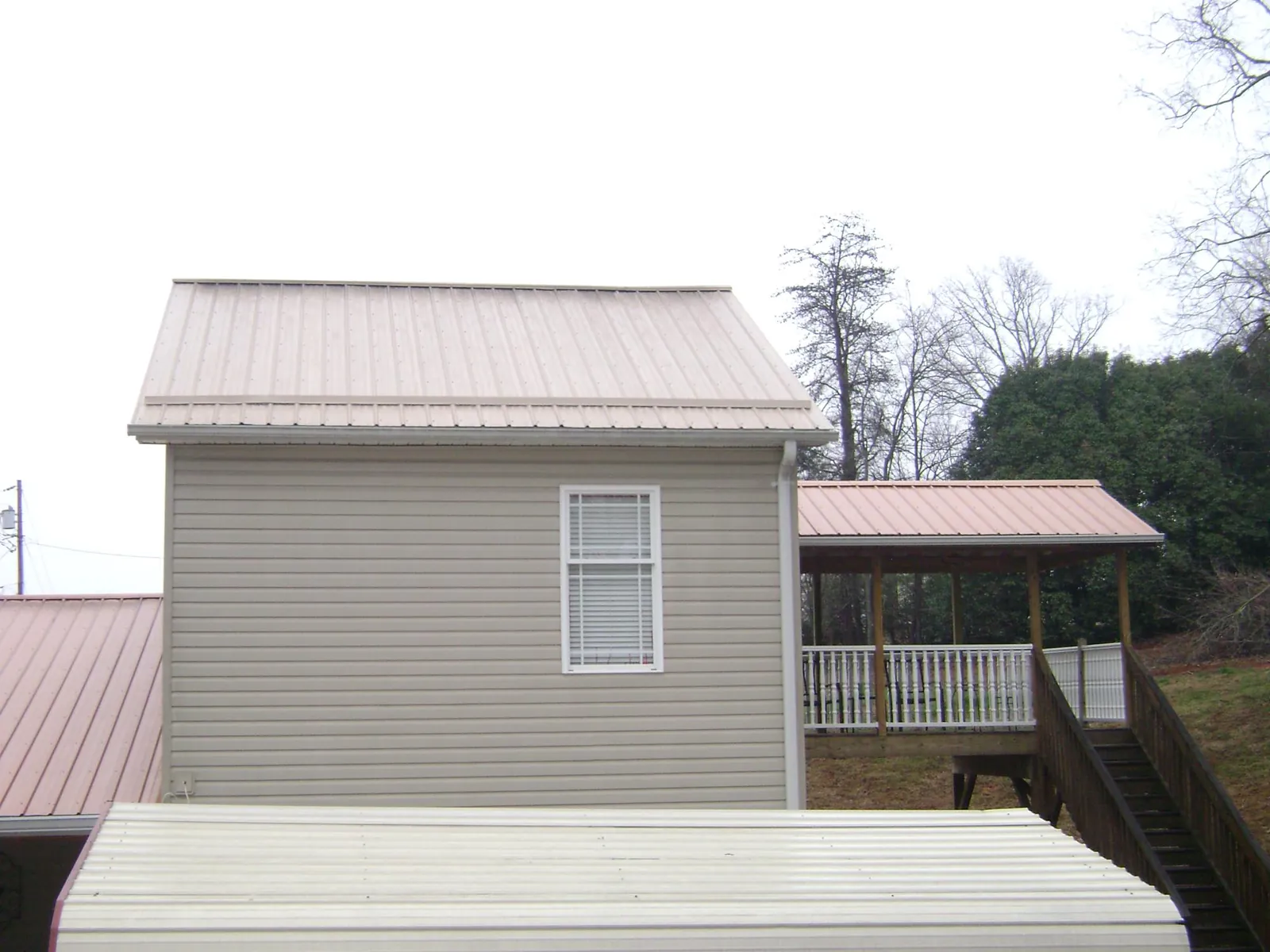 Tan metal roofs on a two story addition and attached porch, from a Roof Replacement job in Williamsville